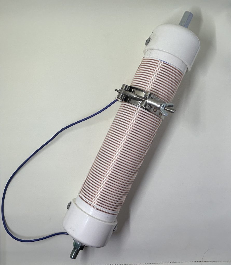 Photograph of loading coil. White PVC form wrapped with copper wire with a wide clamp and a wire lead.