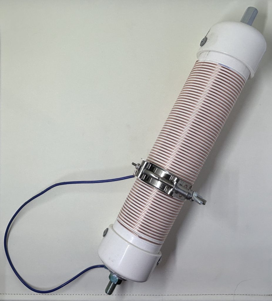 Photograph of loading coil. A PVC form is wrapped with copper wire and an easy to use clamp with a wire connecting to the bottom of the coil. 